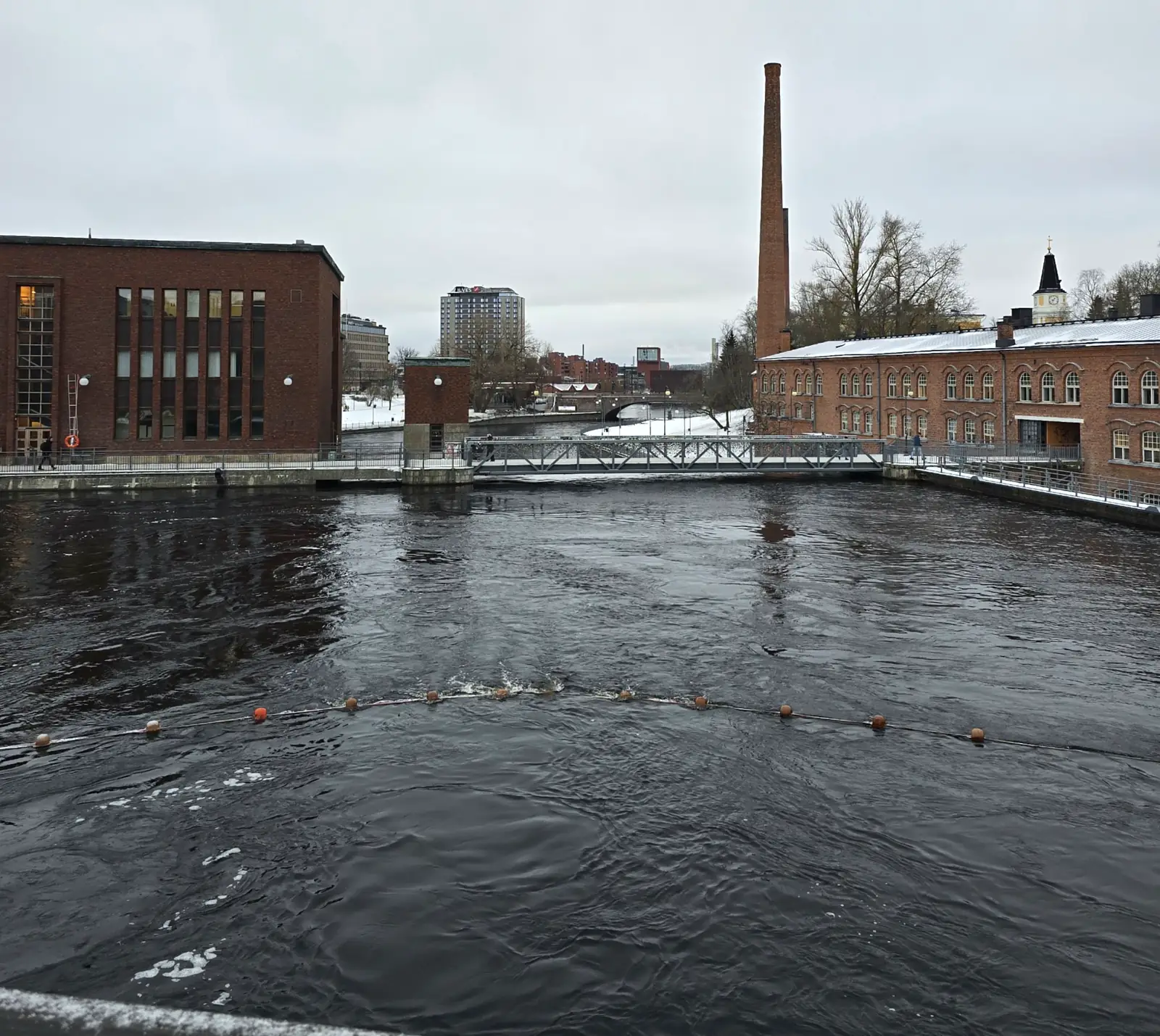 Dark open water of the Tammerkoski rapids flowing through snowy central Tampere