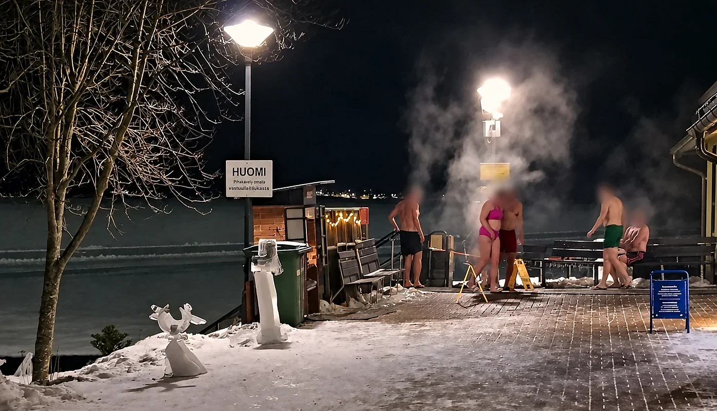 Anonymous winter bathers in steam beside Kaupinoja Sauna and the frozen lake in Tampere