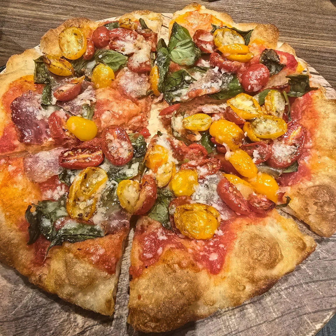 Sapore di Casa pizza with red and yellow tomatoes, basil and capocollo on a wooden board.
