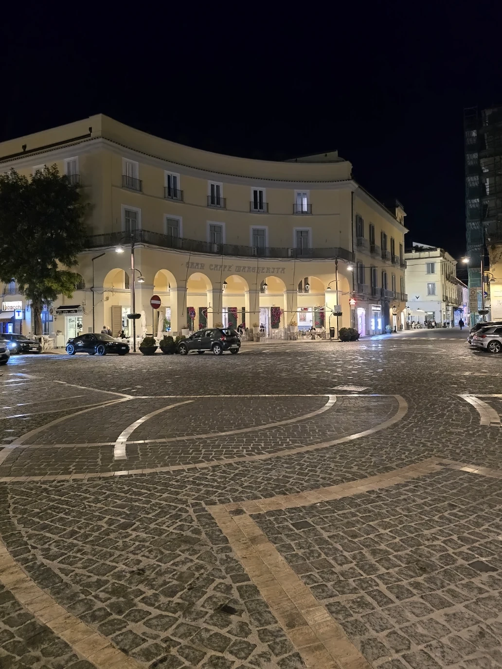 Piazza Dante in Caserta at night, with illuminated arcades and circular patterns in the stone paving.