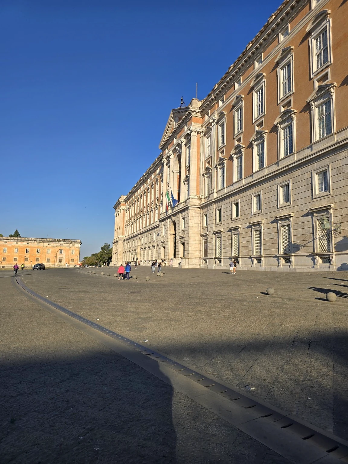 Morning view along the long façade of the Reggia di Caserta, with visitors crossing the square.