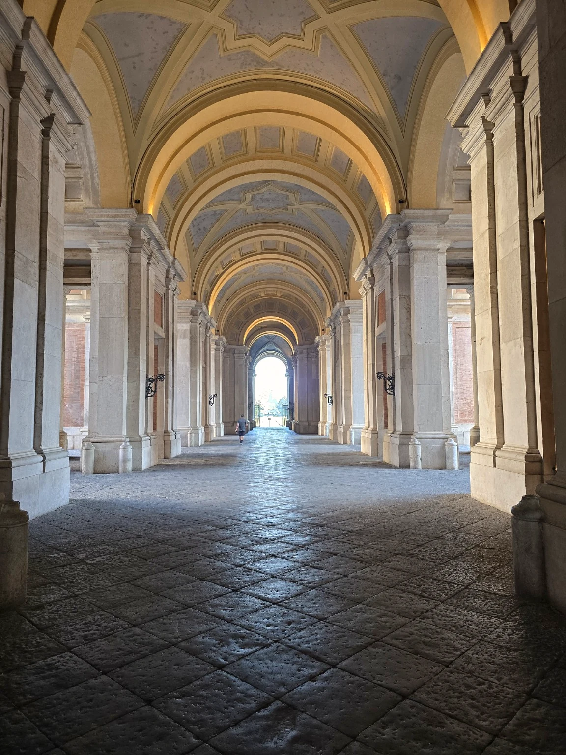Vaulted passage through the Reggia di Caserta, lined with stone columns and light opening towards the park.