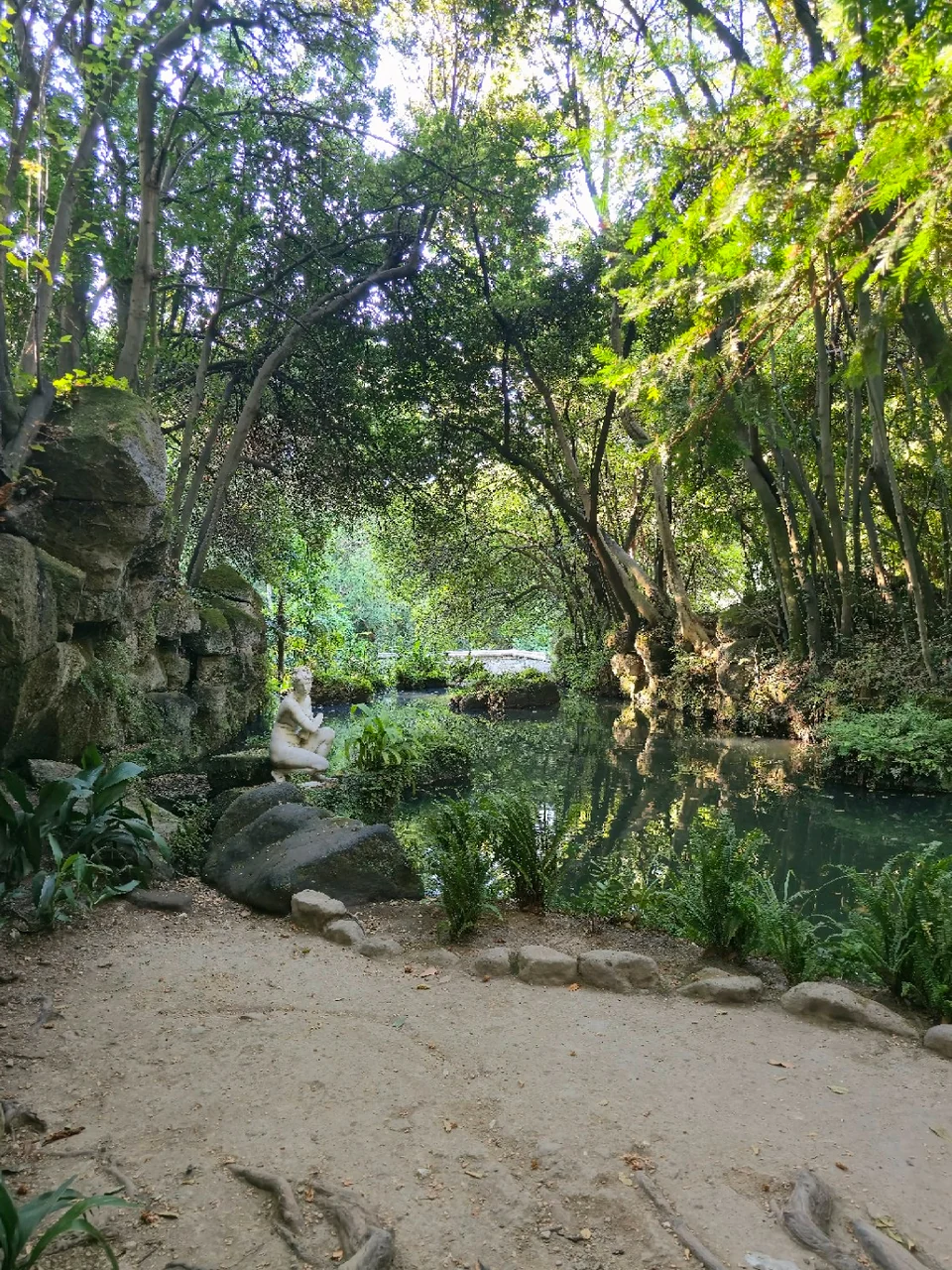 Statue of Venus beside the Bagno di Venere in Caserta, among rocks and greenery by the water.