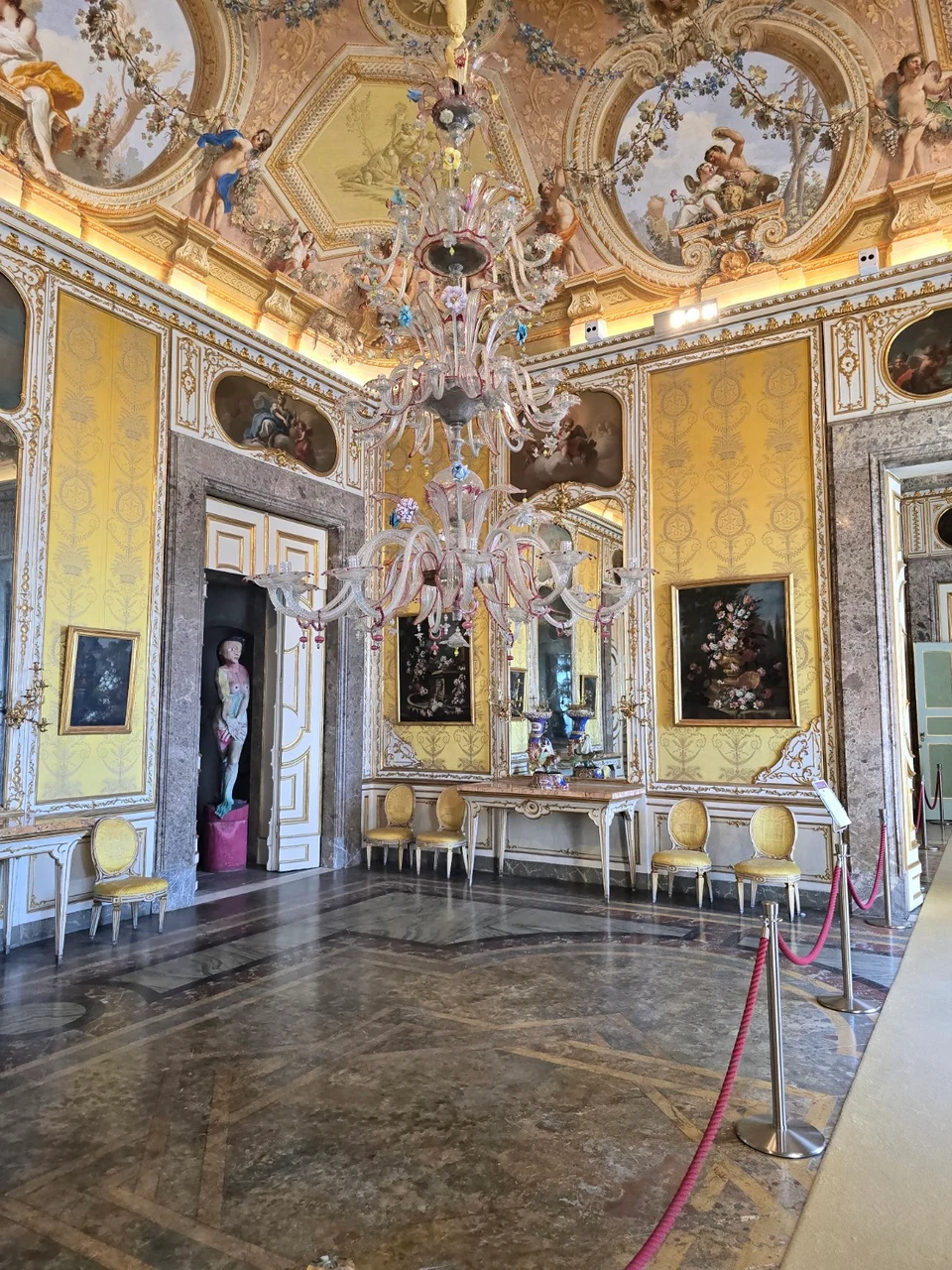 Yellow hall in the Reggia di Caserta with a large glass chandelier and painted ceiling.
