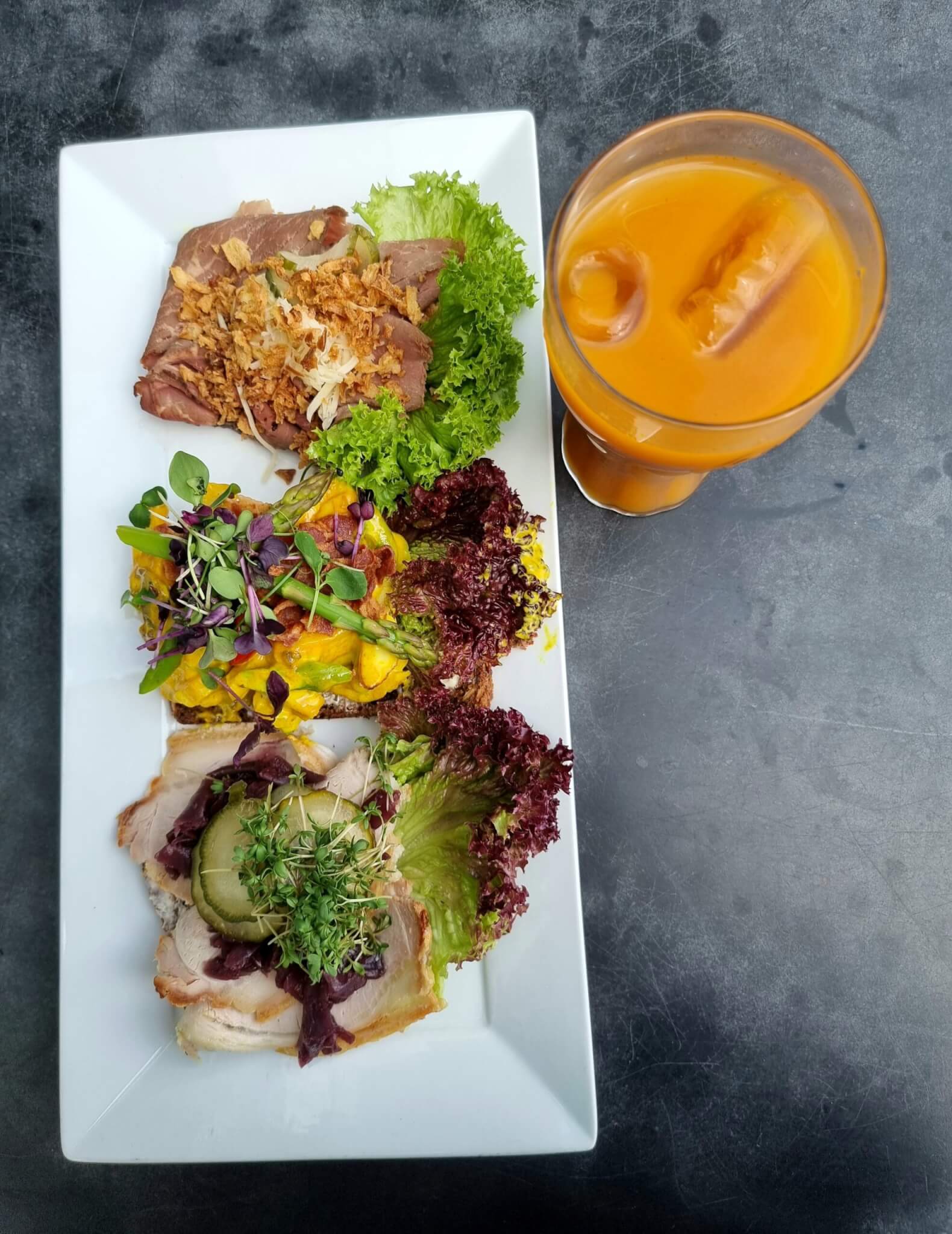 Tri komada danskog smørrebrøda poslužena s narančastim pićem u Helsingøru.