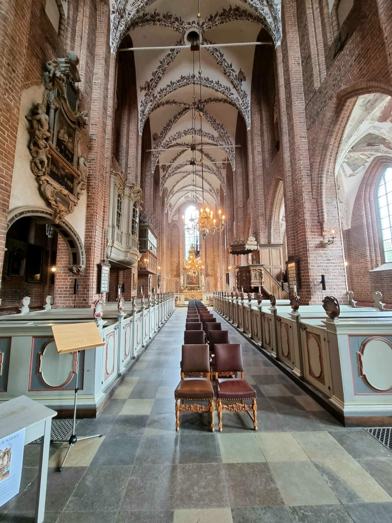 Unutrašnjost crkve sv. Marije u Helsingøru s gotičkim lukovima od opeke, lusterima i oslikanim svodovima.