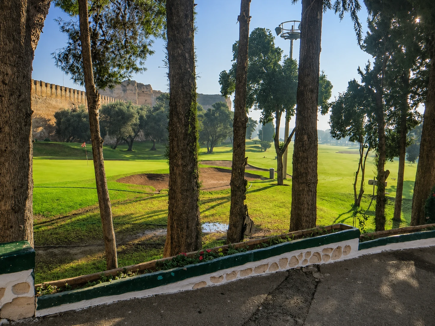 Green golf course framed by trees and bordered by old stone walls at Royal Golf de Meknès.
